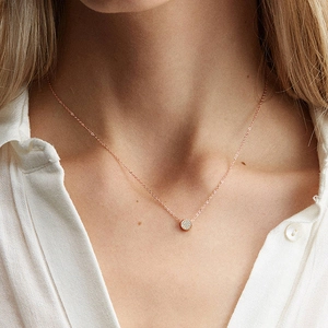 Rose gold round necklace with pavé set diamonds on model wearing white shirt