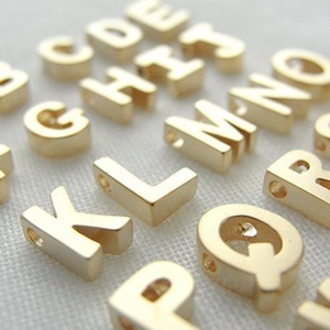 Macro view of gold 316L stainless steel alphabet letter charms with side precision holes