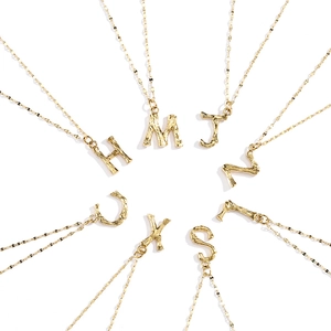 Détail des pendentifs lettres M J Z S X U H dorés à texture bambou sur une chaîne fine