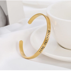 Bracelet jonc en acier doré avec gravure Bites the Dust sur fond minimaliste blanc