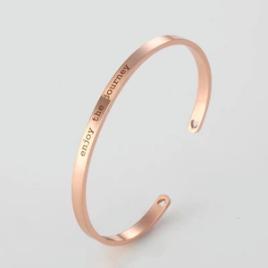 Detail of rose gold stainless steel cuff featuring enjoy the journey text and heart cutouts