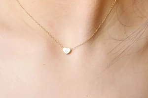Gros plan du collier cœur plaqué or 14K minimaliste avec la lettre G gravée sur la peau