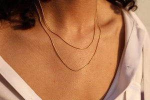 Detail von doppellagigen 14K Gold-Schlangenketten, elegant getragen zum weißen Hemd