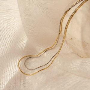 Nahaufnahme goldener und silberner Schlangenketten auf elegantem weißem Leinen