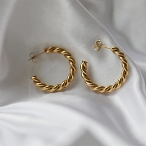 Detailed close-up of C-shaped twisted gold-plated hoop earrings on white silk fabric