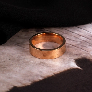 Detailopname van een gepolijste roségouden titanium stalen ring op een getextureerde achtergrond