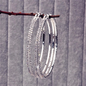 Gros plan de grandes boucles d'oreilles créoles argentées ornées de strass brillants