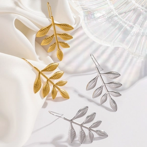 Elegant gold and silver stainless steel leaf earrings displayed on white silk fabric