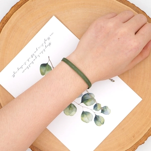Close-up of army green bohemian woven bracelet with silver thread on wooden tray
