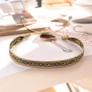 Detail of woven ethnic bracelet with khaki, black, and gold geometric patterns and tassels