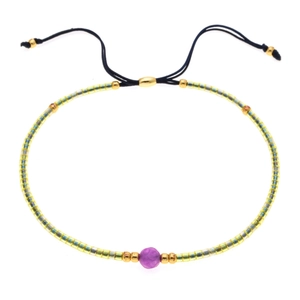 Dettaglio di bracciale intrecciato con perle gialle, pietra viola e cordino regolabile