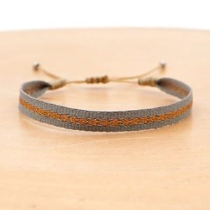 Detail of bohemian woven bracelet with orange geometric embroidery and adjustable pull cord