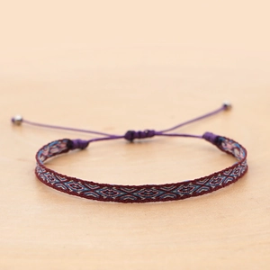 Macro detail of handmade ethnic woven bracelet with burgundy geometric patterns and bead ties