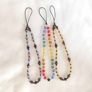 Three acrylic beaded phone lanyards in gray-blue, rainbow, and amber crystal on white fabric