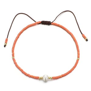 Détail d'un bracelet tressé à la main avec perles orange, perle blanche et cordon