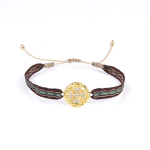 Détail d'un bracelet ethnique tissé à la main avec pendentif croix dorée et cordon réglable