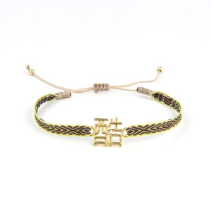 Détail d'un bracelet ethnique tressé avec un charm doré portant le caractère chinois Ku