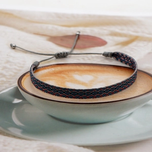 Ethnic woven bracelet in red and blue patterns displayed on a coffee cup with latte art