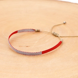 Macro detail of hand-woven bohemian bracelet with red thread and metallic accents