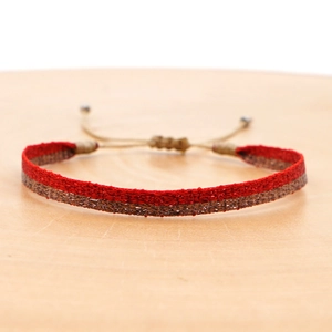 Close-up of handmade woven bohemian bracelet in red and bronze on a wooden surface