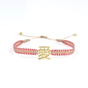 Détail du bracelet tissé main avec cordon rouge et blanc et breloque dorée 'Amour'