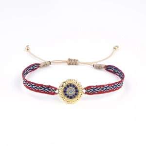Détail d'un bracelet ethnique tissé main avec un motif œil turc en métal doré central