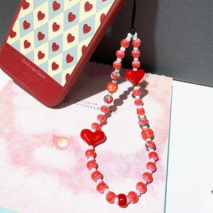 Handmade beaded phone strap with red acrylic hearts and floral patterns on pink notebook