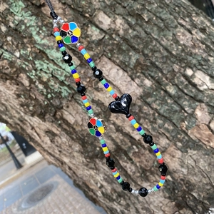 Colorful beaded phone strap with peace flower and heart pendant on tree bark background