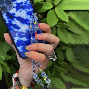 Cordon de téléphone en perles irisées avec coque tie-dye bleue tenu à la main au jardin
