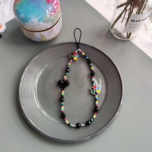 Colorful beaded phone charm with black heart and peace sign sunflower pendants in a ceramic tray