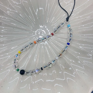 Handmade clear crystal beaded phone strap with colorful accent beads in a ceramic tray
