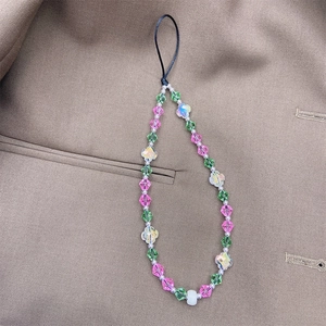 Detail of colorful crystal phone strap with green and pink beads on brown fabric