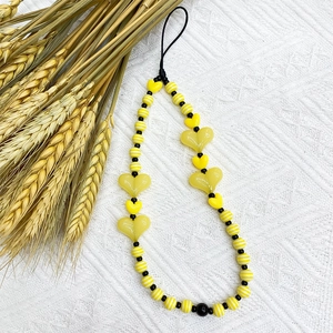 Acrylic yellow heart and striped bead phone wrist lanyard on white fabric background