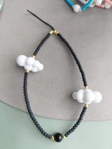 Detail of beaded mobile phone strap featuring white cloud charms and matte black beads