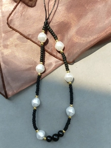 Detail of baroque pearl phone strap with matte black beads and golden spacers