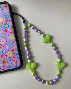 Detail of beaded phone strap with green hearts and purple striped beads on a stone surface