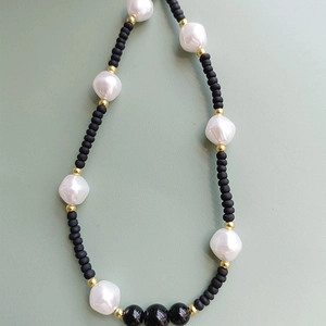 Baroque pearl and black bead mobile chain with golden spacers on neutral background
