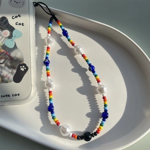 Colorful beaded phone strap with white faux pearls and blue evil eye charms on a tray