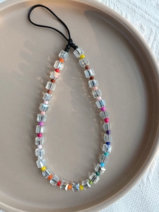 Detailed macro view of colorful crystal cube phone charm strap on a ceramic tray