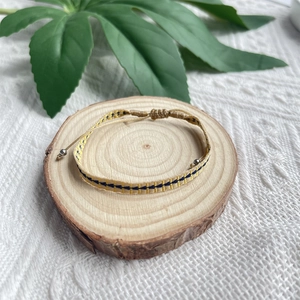 Détail d'un bracelet bohème tressé main jaune avec motifs bleus sur support en bois