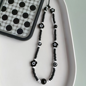Detail of beaded phone strap featuring black floral accents and evil eye beads