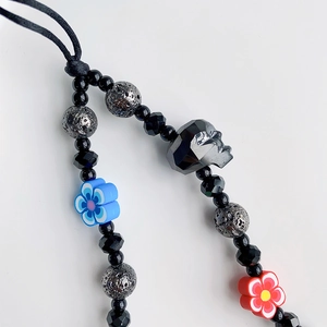 Macro detail of a beaded phone strap with black skull bead and colorful clay flowers