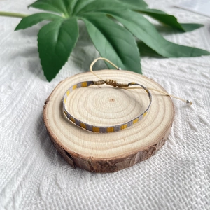 Détail du bracelet tressé jaune et gris avec nœud ajustable sur fond de bois naturel