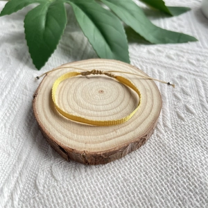 Détail du bracelet bohème jaune tissé à la main avec cordon réglable sur fond de bois naturel