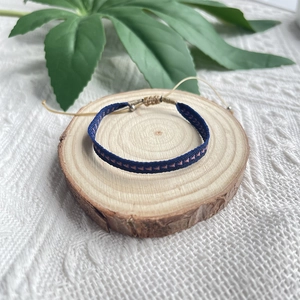 Bracelet tressé bohème bleu marine à motifs géométriques sur un socle en bois rustique