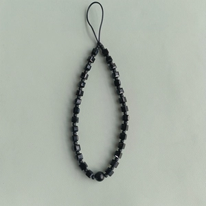 Minimalist black faceted square bead phone strap with circular bead accent on textured surface