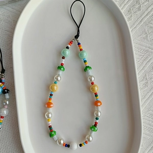 Close-up of colorful beaded phone wrist strap featuring a red polka dot mushroom charm
