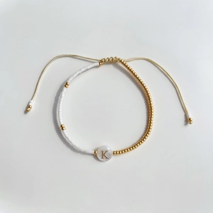 Detail van kralenarmband met gouden kralen en verstelbaar koord met de letter K erop