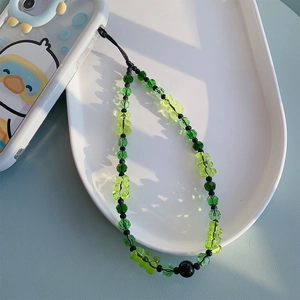 Détail de la dragonne de téléphone avec oursons en gomme et perles vertes sur plateau