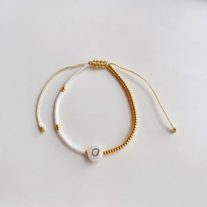 Detailopname van kralenarmband met gouden TOHO-kralen en wit bedeltje met letter O